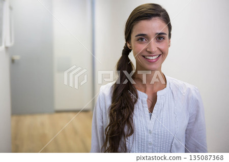 Woman in twenties standing in lit corridor wearing button-up blouse by frosted door, copy space 135087368