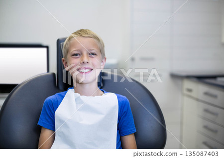 Child patient sitting on reclining dental chair in treatment room wearing protective bib by monitor Child patient sitting on reclining dental chair in treatment room wearing protective bib by monitor 135087403