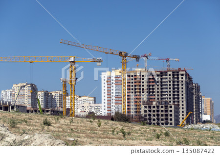 New residential district under construction in Novorossiysk, Russia, with unfinished monolithic apartment buildings and tower cranes against the sky 135087422