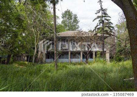 Old abandoned two-story house made of white brick, showing decay, neglect and architectural details, representing urban ruin and forgotten residential buildings 135087469