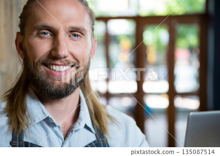 Middle-aged man standing behind cafe counter with laptop and wearing dark apron, copy space Middle-aged man standing behind cafe counter with laptop and wearing dark apron, copy space 135087514