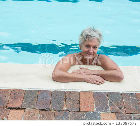 Senior woman resting on pool coping at backyard pool deck with turquoise water and brick pavers Senior woman resting on pool coping at backyard pool deck with turquoise water and brick pavers 135087572