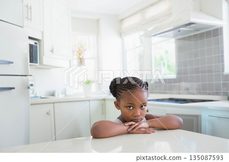 Child African American girl leaning on island looking thoughtful in kitchen near white cabinets Child African American girl leaning on island looking thoughtful in kitchen near white cabinets 135087593