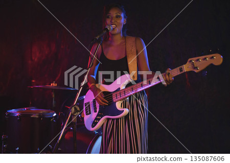 African American woman musician performing on stage singing into microphone and playing bass guitar 135087606