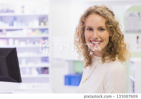 Female pharmacy staff smiling while checking computer monitor and organizing shelves, copy space Female pharmacy staff smiling while checking computer monitor and organizing shelves, copy space 135087609
