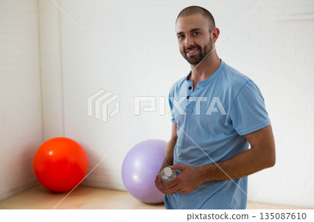 Man holding water bottle near red and lavender stability balls in fitness studio, copy space 135087610