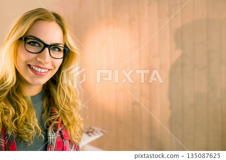 Woman smiling wearing glasses, plaid shirt beside wood wall by white table with photos, copy space Woman smiling wearing glasses, plaid shirt beside wood wall by white table with photos, copy space 135087625