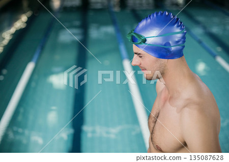 Male swimmer standing at pool edge near lanes wearing blue cap and green goggles, copy space Male swimmer standing at pool edge near lanes wearing blue cap and green goggles, copy space 135087628