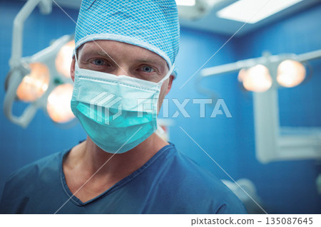 Middle-aged man standing in operating theatre wearing scrubs mask under surgical lights 135087645