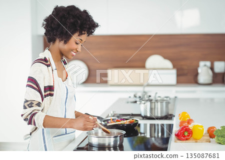 African American woman stirring pot on cooktop next to bell peppers in modern kitchen, copy space African American woman stirring pot on cooktop next to bell peppers in modern kitchen, copy space 135087681