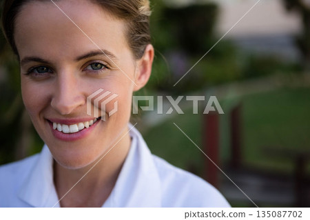 Woman smiling broadly in white collared coat outdoors in home garden with wooden posts 135087702