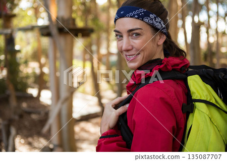 Female hiker standing on trail wearing red jacket, blue bandana, carrying green backpack near ropes Female hiker standing on trail wearing red jacket, blue bandana, carrying green backpack near ropes 135087707