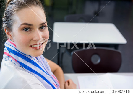 Female student with striped towel smiling while writing in notebook at school desk, copy space 135087716