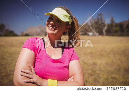 Mid adult woman standing in field wearing pink athletic shirt yellow wristband and yellow visor Mid adult woman standing in field wearing pink athletic shirt yellow wristband and yellow visor 135087720