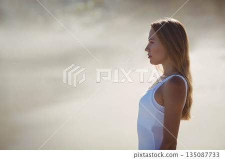 Woman wearing white tank top standing at shoreline, facing right and watching waves, copy space Woman wearing white tank top standing at shoreline, facing right and watching waves, copy space 135087733