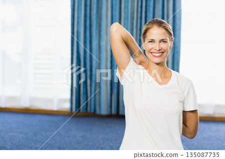 Woman stretching shoulder at home in front of window with blue drapes and carpet, copy space 135087735