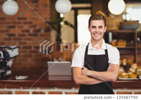 Male barista wearing apron behind cafe counter crossing arms near espresso machine, copy space Male barista wearing apron behind cafe counter crossing arms near espresso machine, copy space 135087750