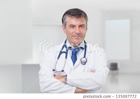 Male doctor standing arms crossed in clinic wearing lab coat, blue tie, stethoscope and wristwatch 135087772