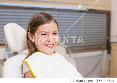 Female child patient sitting in dental clinic chair wearing bib smiling and waiting for care Female child patient sitting in dental clinic chair wearing bib smiling and waiting for care 135087785