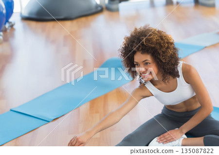 African American woman stretching on blue yoga mat in studio with exercise balls, mats, copy space 135087822