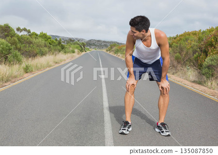Male runner pausing on centerline of rural road in athletic clothing and running shoes, copy space Male runner pausing on centerline of rural road in athletic clothing and running shoes, copy space 135087850