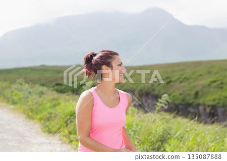 Woman jogging along gravel trail through grassy hillside wearing pink tank top, copy space Woman jogging along gravel trail through grassy hillside wearing pink tank top, copy space 135087888