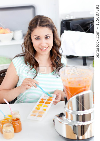 Woman standing behind kitchen counter using pastel blue spoon filling sectioned tray with purees 135087893