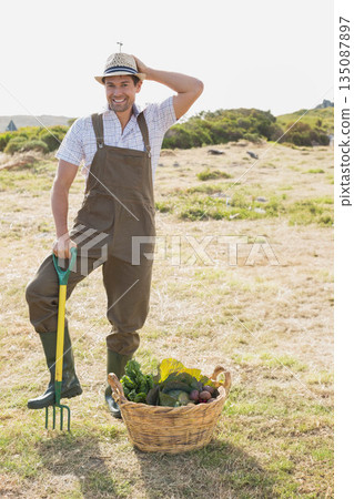 Man standing behind wicker basket holding pitchfork in dry field harvesting seasonal vegetables 135087897