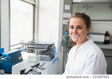 Female scientist wearing lab coat examining under microscope at bench with trays, copy space Female scientist wearing lab coat examining under microscope at bench with trays, copy space 135087903