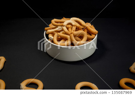 Crispy small breadsticks served on a white glass plate against a black background. Minimalistic food composition highlighting texture, contrast, and simple snack presentation. 135087969