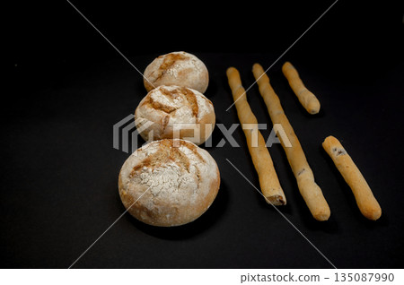 Top-view shot of freshly baked whole grain buns on a black background. Rustic homemade bread texture with seeds and golden crust, showcasing artisanal baking and healthy food. Concept for bakery. Top-view shot of freshly baked whole grain buns on a black background. Rustic homemade bread texture with seeds and golden crust, showcasing artisanal baking and healthy food. Concept for bakery. 135087990