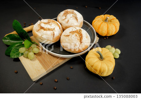 Autumn still life with pumpkins and homemade freshly baked buns arranged on a black background. Warm rustic mood, seasonal harvest, cozy food concept. Autumn still life with pumpkins and homemade freshly baked buns arranged on a black background. Warm rustic mood, seasonal harvest, cozy food concept. 135088003