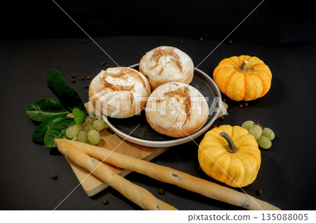 Autumn still life with pumpkins and homemade freshly baked buns arranged on a black background. Warm rustic mood, seasonal harvest, cozy food concept. Autumn still life with pumpkins and homemade freshly baked buns arranged on a black background. Warm rustic mood, seasonal harvest, cozy food concept. 135088005