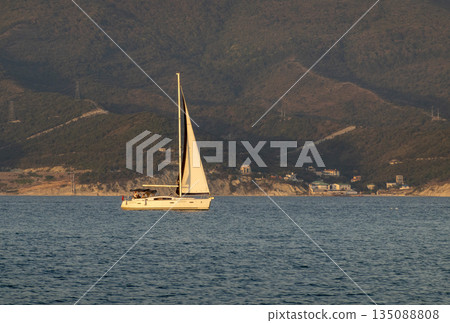 August 22 2025 Sailing yacht with white sail on the Black Sea near Novorossiysk Russia. Recreational yacht moving along the coastline. 135088808