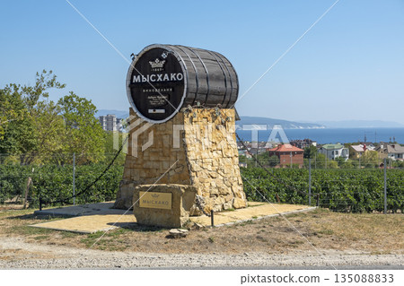August 24, 2025: Genre sculpture of a barrel with winery sign in Myskhako, Russia, with the sea and mountains on the horizon, symbolizing local winemaking, tourism and coastal landscape August 24, 2025: Genre sculpture of a barrel with winery sign in Myskhako, Russia, with the sea and mountains on the horizon, symbolizing local winemaking, tourism and coastal landscape 135088833