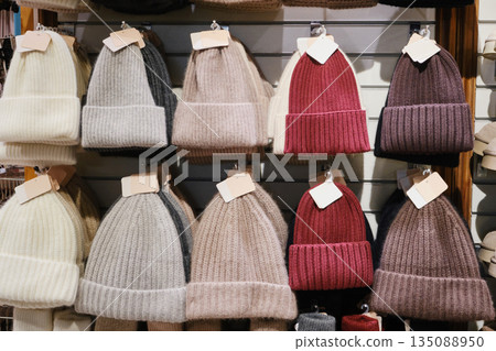 Knitted winter wool beanies hanging on display for sale in fashion store Knitted winter wool beanies hanging on display for sale in fashion store 135088950