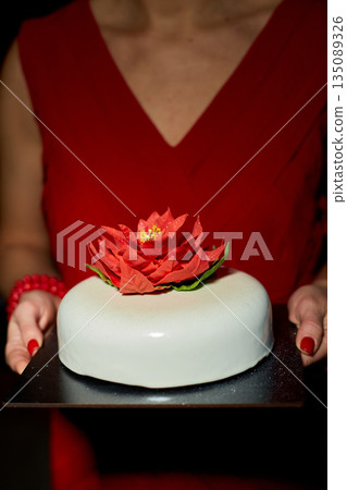 A Person Holding a Beautifully Decorated Cake Adorned With a Vibrant Flower in a Dimly Lit Setting During a Special Celebration 135089326