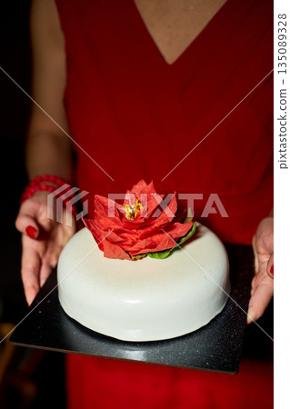 A Person Holding a Beautifully Decorated Cake Adorned With a Vibrant Flower in a Dimly Lit Setting During a Special Celebration 135089328