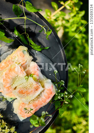 Fresh spring rolls served on a decorative tray surrounded by greenery in a vibrant outdoor setting Fresh spring rolls served on a decorative tray surrounded by greenery in a vibrant outdoor setting 135089334