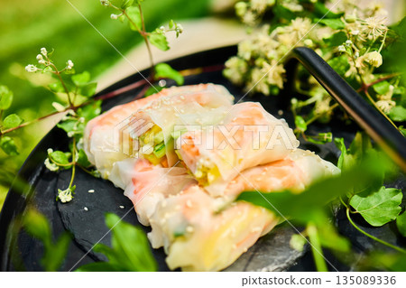 Fresh spring rolls served on a decorative tray surrounded by greenery in a vibrant outdoor setting 135089336