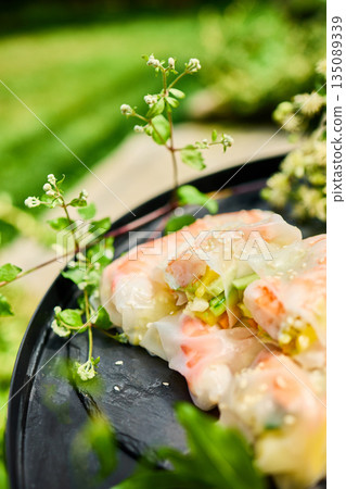 Fresh spring rolls served on a decorative tray surrounded by greenery in a vibrant outdoor setting Fresh spring rolls served on a decorative tray surrounded by greenery in a vibrant outdoor setting 135089339