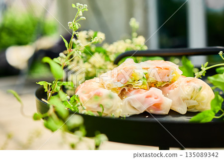 Fresh spring rolls served on a decorative tray surrounded by greenery in a vibrant outdoor setting Fresh spring rolls served on a decorative tray surrounded by greenery in a vibrant outdoor setting 135089342