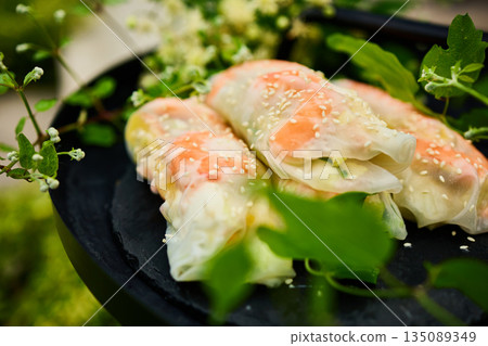 Fresh spring rolls served on a decorative tray surrounded by greenery in a vibrant outdoor setting 135089349