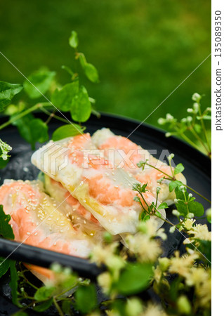Fresh spring rolls served on a decorative tray surrounded by greenery in a vibrant outdoor setting 135089350