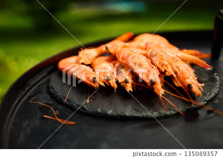 Grilled shrimp on a black grill plate surrounded by green grass in a sunny outdoor setting Grilled shrimp on a black grill plate surrounded by green grass in a sunny outdoor setting 135089357