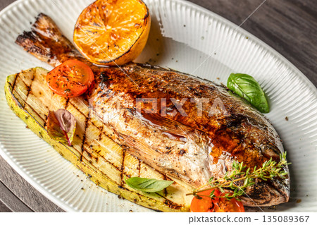 grilled whole dorado fish with vegetables and lemon on a white plate. top view 135089367