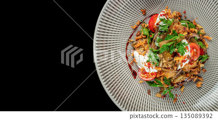 Grilled eggplant salad with tomatoes, fresh herbs, crispy onions, and yogurt sauce on a gray plate. top view. copy space Grilled eggplant salad with tomatoes, fresh herbs, crispy onions, and yogurt sauce on a gray plate. top view. copy space 135089392