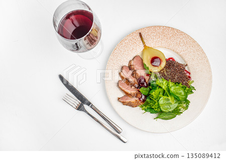 Duck breast with berry sauce, poached pear, fresh greens, and a glass of red wine on a white background. copy space, top view Duck breast with berry sauce, poached pear, fresh greens, and a glass of red wine on a white background. copy space, top view 135089412