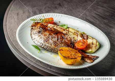 Grilled dorado fish with vegetables and lemon on a plate Grilled dorado fish with vegetables and lemon on a plate 135089430