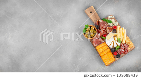 Antipasto board with assorted cheeses, cured meats, crackers, figs, olives, and fresh berries on a rustic wooden serving board, top view, copy space Antipasto board with assorted cheeses, cured meats, crackers, figs, olives, and fresh berries on a rustic wooden serving board, top view, copy space 135089439